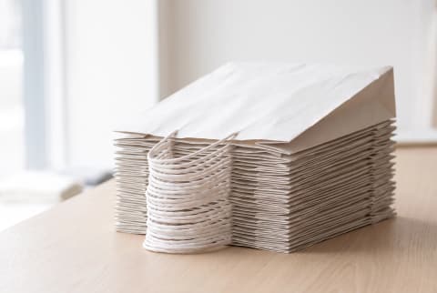 A neat stack of plain white kraft paper bags folded flat, handles folded down