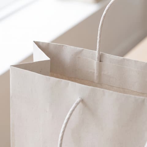 Close-up of a plain white kraft paper bag: folded top edge and a twisted paper handle glued inside