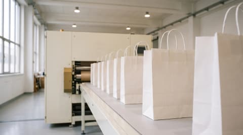 Finished plain white paper bags with twisted handles in a row on a conveyor